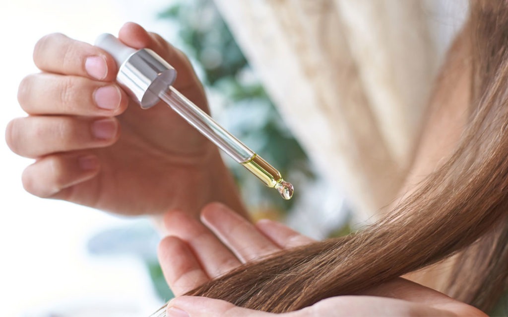 Photo showing a dropper of hair damage treatment oil, and strands of healthy hair as a result of the treatment.