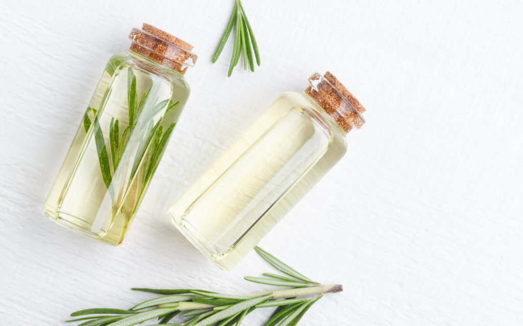 Photo showing sprigs of rosemary and two bottles of the hair thickening essential oil treatment made from it.