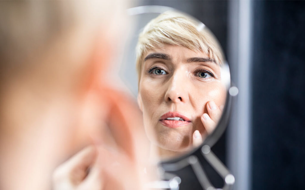Photo of woman looking in mirror at smoother skin, noticing that her telomeres are helping to reduce wrinkles.