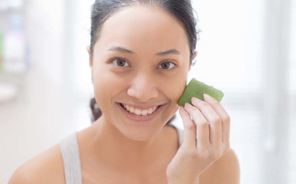 Photo showing a woman applying aloe vera leaf to moisturize her clean skin.