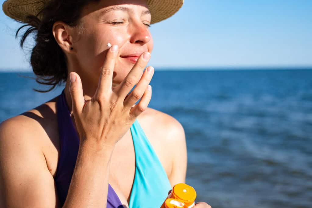 Midlife or mature woman (40s–60s) outdoors, applying SPF 